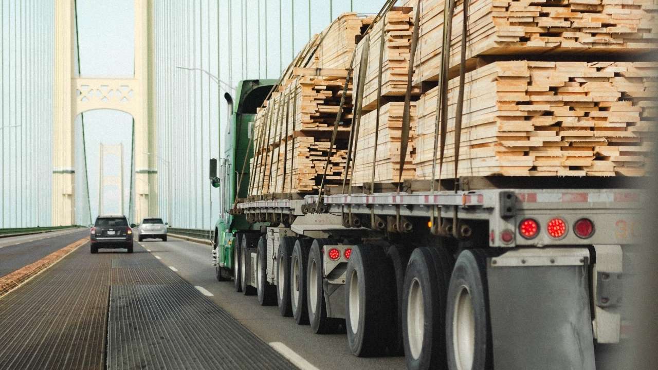 Green truck with wood cargo driving on a bridge